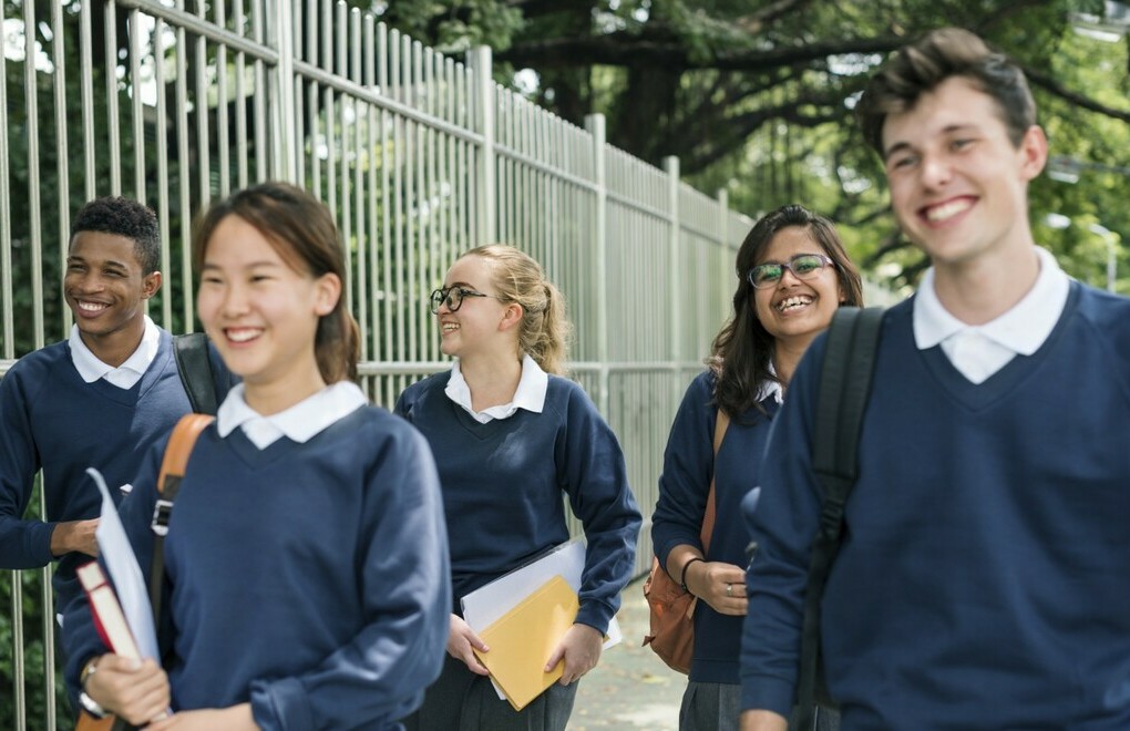 Students walking beside a fence in school uniforms